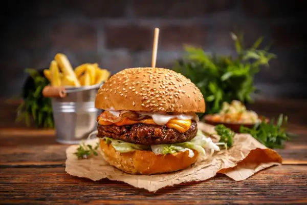 Soczysty burger wołowy z serem, bekonem i frytkami na drewnianym stole.